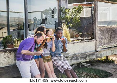 Stock Photo - Friends eating watermelon in backyard. Fotosearch
