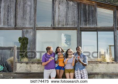 Stock Photography - Friends eating watermelon in backyard. Fotosearch