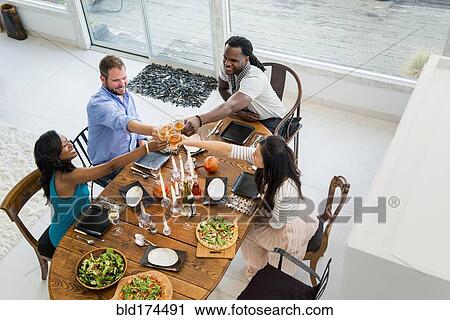 Stock Image - Friends toasting at dining room table. Fotosearch