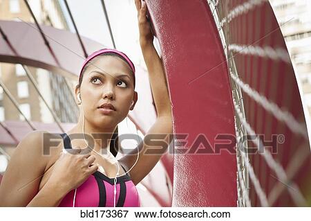 Stock Photo - Hispanic woman listening to headphones under structure. Fotosearch