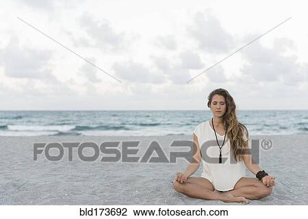 Stock Image - Hispanic woman meditating on beach. Fotosearch