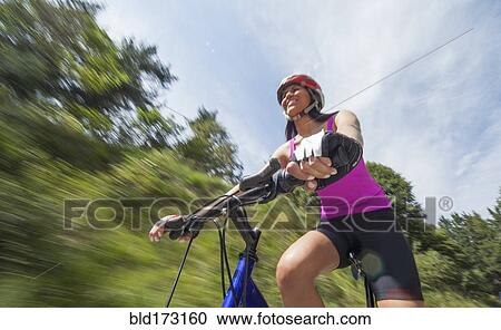 Stock Image - Hispanic woman riding bicycle outdoors. Fotosearch