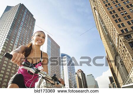 Hispanic woman riding bicycle under highrise buildings View Large Photo Image Stock Photo - Hispanic woman riding bicycle under highrise buildings. Fotosearch