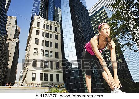 Stock Image - Hispanic woman stretching under highrise buildings. Fotosearch