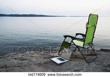 Stock Photo - Laptop on lawn chair near remote river. Fotosearch
