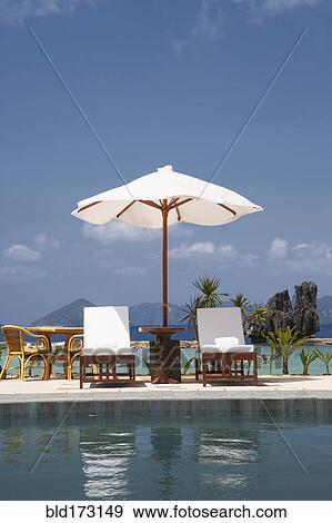 Stock Photo - Lawn chair and umbrella at swimming pool. Fotosearch