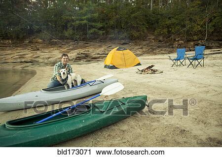 Stock Image - Man and dog with kayak at campsite. Fotosearch
