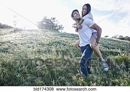 Stock Photo - Man carrying girlfriend piggyback in field. Fotosearch