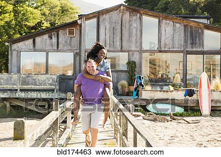 Man carrying girlfriend piggyback on wooden deck View Large Photo Image Stock Image - Man carrying girlfriend piggyback on wooden deck. Fotosearch