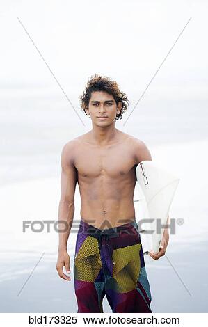 Stock Photography - Man carrying surfboard on beach. Fotosearch