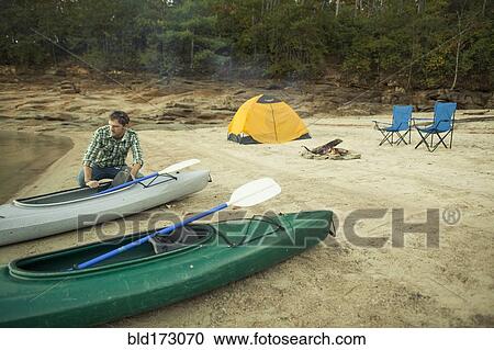 Stock Image - Man pushing kayak into lake. Fotosearch