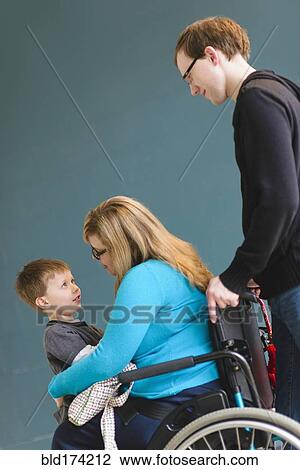 Stock Image - Man pushing paraplegic wife and son. Fotosearch
