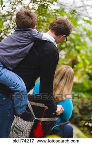 Stock Photo - Man pushing paraplegic wife and carrying son piggyback. Fotosearch