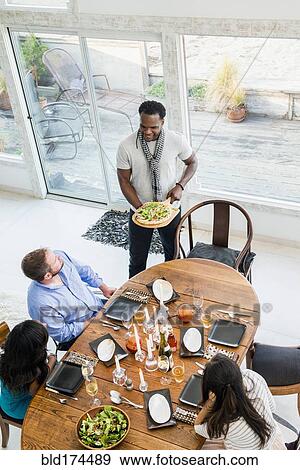 Stock Photo - Man serving friends at dinner party. Fotosearch