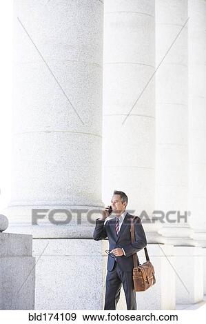 Mixed race businessman talking on cell phone under columns View Large Photo Image Stock Photo - Mixed race businessman talking on cell phone under columns. Fotosearch