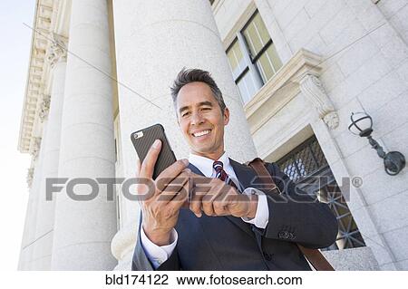 Stock Image - Mixed race businessman using cell phone outside courthouse. Fotosearch