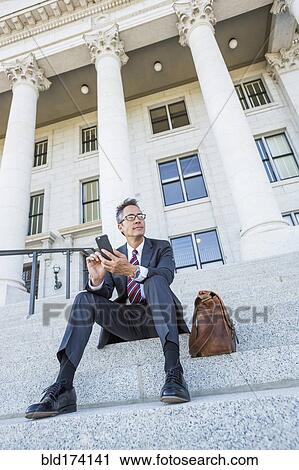 Stock Image - Mixed race businessman using cell phone on courthouse steps. Fotosearch