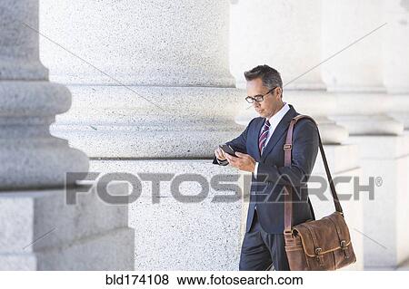 Stock Photo - Mixed race businessman using cell phone under columns. Fotosearch