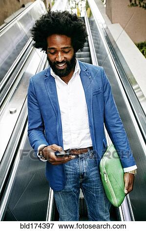 Mixed race businessman using cell phone on escalator View Large Photo Image Stock Photo - Mixed race businessman using cell phone on escalator. Fotosearch