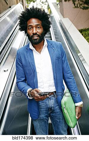 Stock Photo - Mixed race businessman using cell phone on escalator. Fotosearch