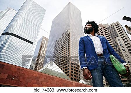 Stock Image - Mixed race businessman walking under skyscrapers. Fotosearch