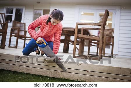 Stock Photo - Mixed race girl sawing wood in backyard. Fotosearch
