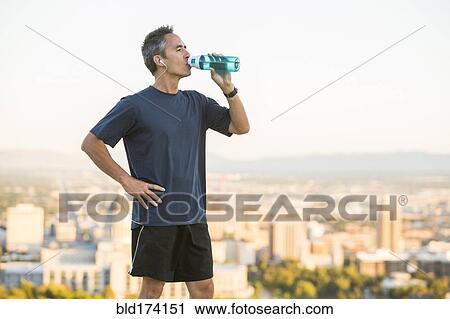Stock Image - Mixed race man drinking water bottle on urban hilltop. Fotosearch