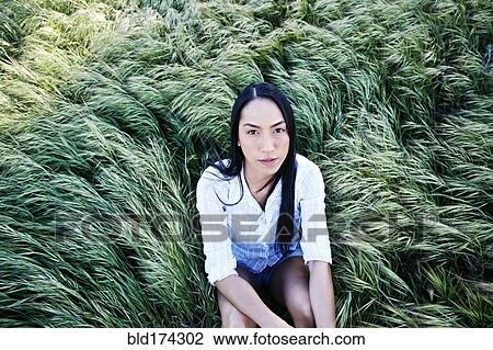 Stock Image - Mixed race woman sitting in grass. Fotosearch