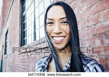 Stock Photo - Mixed race woman smiling at brick wall. Fotosearch