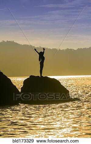 Stock Photo - Mixed race woman standing on rock over ocean. Fotosearch