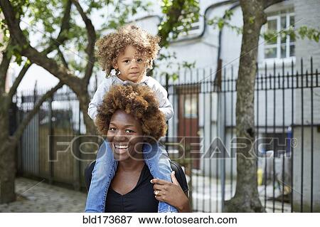 Stock Photo - Mother carrying daughter on shoulders outdoors. Fotosearch