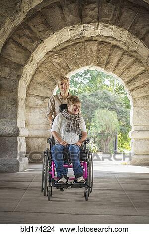 Picture - Mother pushing paraplegic daughter in wheelchair. Fotosearch