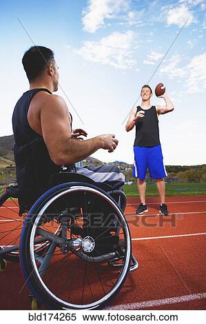 Stock Photography - Paraplegic athlete in wheelchair tossing ball with friend. Fotosearch