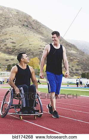 Stock Photo - Paraplegic athlete in wheelchair with friend on track. Fotosearch