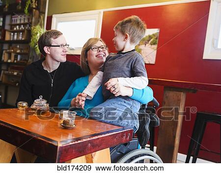 Stock Photo - Paraplegic mother holding son in tea shop. Fotosearch
