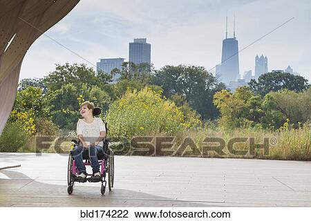 Stock Image - Paraplegic woman sitting in wheelchair under city skyline. Fotosearch