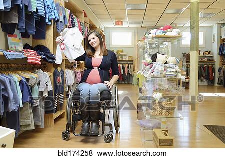 Stock Photo - Pregnant paraplegic woman in wheelchair shopping in baby store. Fotosearch