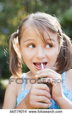 Picture - Smiling girl eating candy cigarette in backyard. Fotosearch