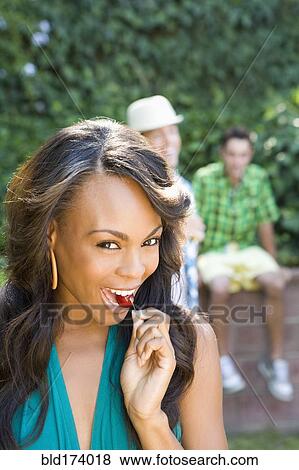 Stock Photo - Smiling woman eating cherry in backyard. Fotosearch