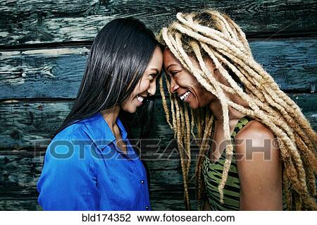 Stock Image - Smiling women touching foreheads at wooden wall. Fotosearch