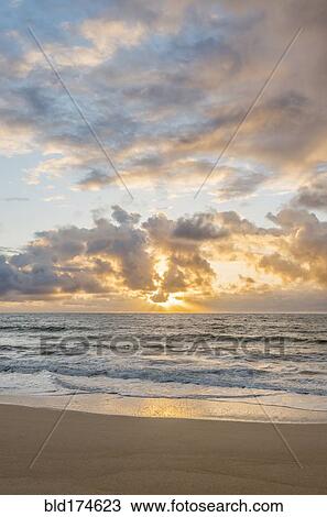 Stock Image - Sunrise over ocean on beach. Fotosearch