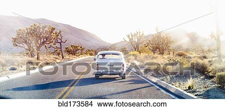 Picture - Vintage car driving on desert road. Fotosearch