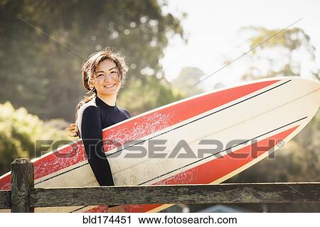 Stock Image - Woman carrying surfboard outdoors. Fotosearch