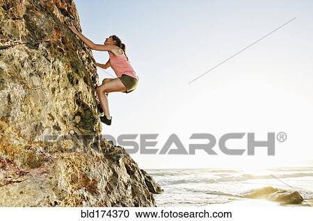 Stock Image - Woman climbing rock formation. Fotosearch