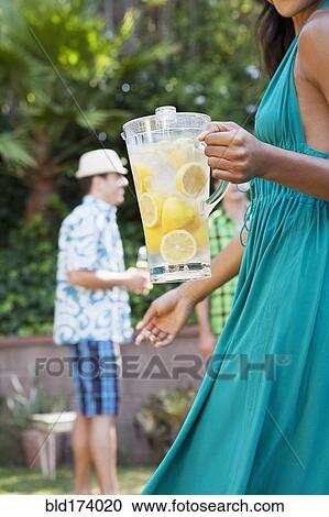Stock Image - Woman holding pitcher of lemonade at backyard barbecue. Fotosearch