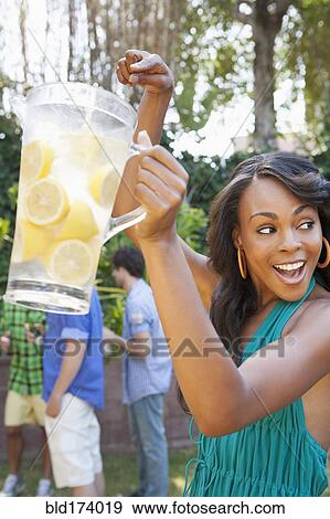 Stock Photo - Woman holding pitcher of lemonade at backyard barbecue. Fotosearch
