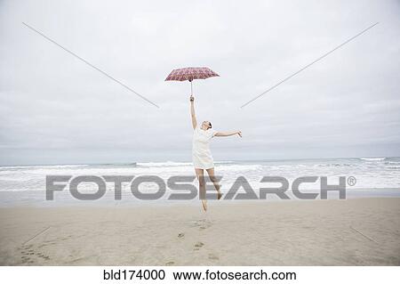 Stock Image - Woman playing with umbrella on beach. Fotosearch