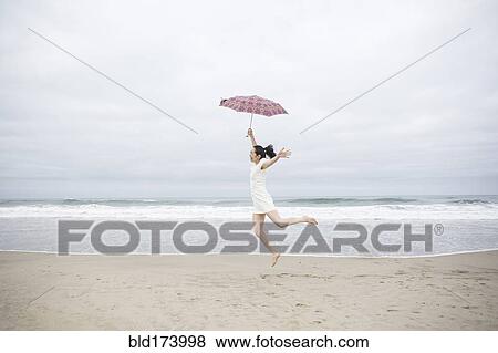 Stock Photo - Woman playing with umbrella on beach. Fotosearch