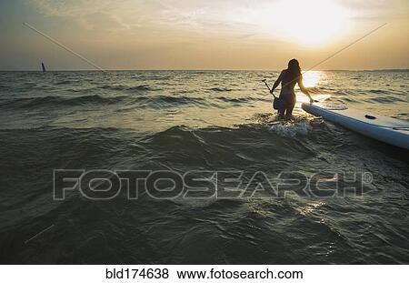 Stock Photo - Woman pulling paddleboard in lake. Fotosearch
