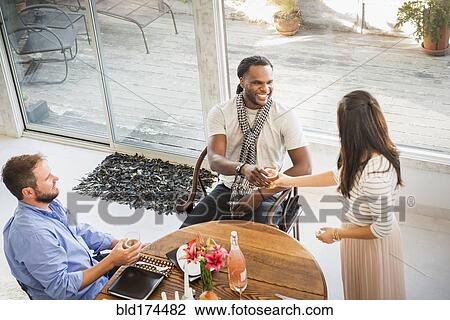 Stock Image - Woman serving friend at dinner party. Fotosearch